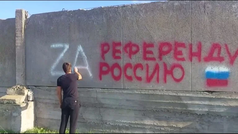 В місті на Херсонщині якісь люди псують паркани заради «картинки» для пропагандистів Хлопець наносить напис на стіну