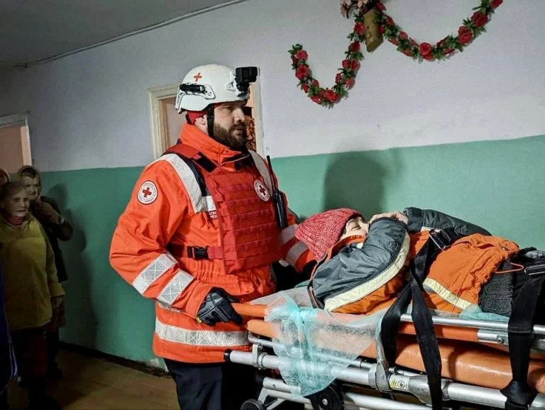 Волонтер Червоного Хреста везе жінку на носилках