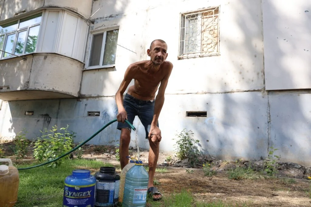 Дуже худий чоловік набирає воду у пластикові ємності  