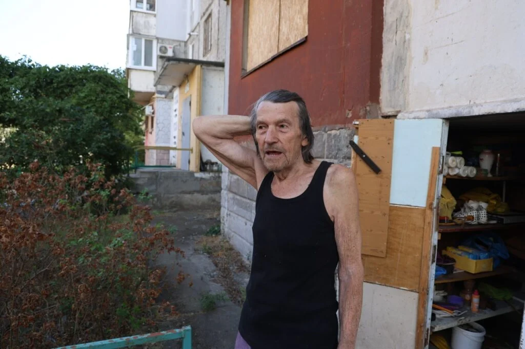 Чоловік у майці стоїть біля будинку