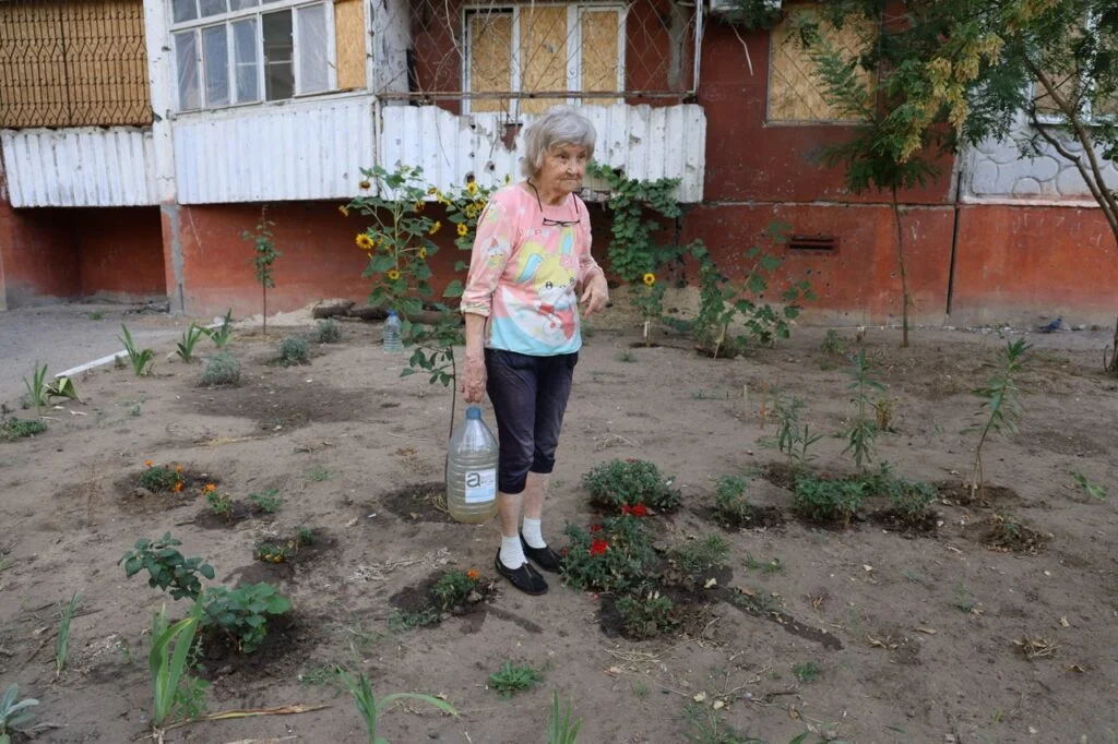 Літня жінка поливає квіти