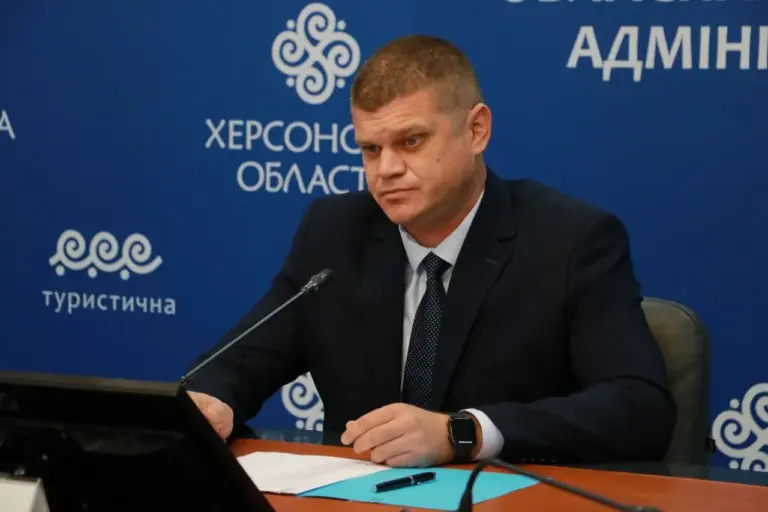 Чоловік у костюмі сидить за столом із мікрофоном
