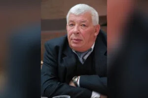 Літній чоловік у темному піджаку сидить за столом