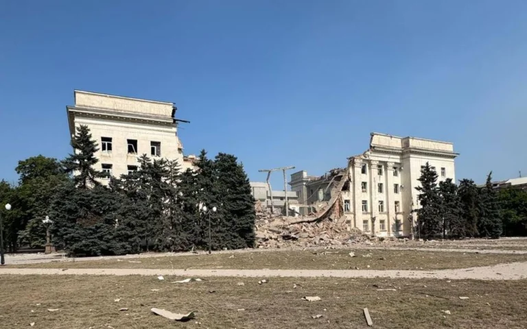 Пошкоджена багатоповерхова будівля з уламками перед фасадом
