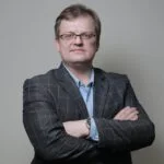 Чоловік в окулярах стоїть зі схрещеними руками