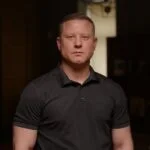 Чоловік у чорній сорочці дивиться в камеру