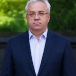 Чоловік у темному костюмі на тлі зелені