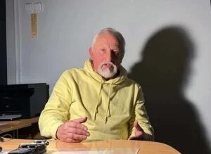 Літній чоловік у жовтому худі сидить за столом