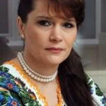 Жінка у вишиванці та намисті дивиться в камеру
