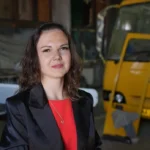Жінка позує в приміщенні на тлі жовтого транспорту