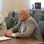 Чоловік у сірому піджаку сидить за столом засідань